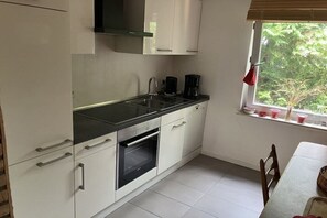 A kitchen with white cabinets, a black countertop, a built-in oven, a sink, and a window with a view of greenery. - with garden and fireplace (Geeste)