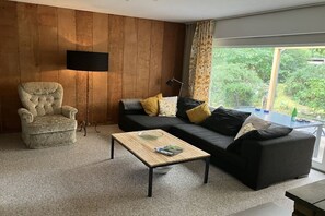 A living room with a sofa, armchair, coffee table, and a flat-screen TV mounted on a wooden wall. - with garden and fireplace (Geeste)