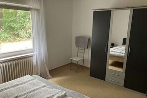 A bedroom with a bed, a wardrobe, a chair, and a window. - with garden and fireplace (Geeste)