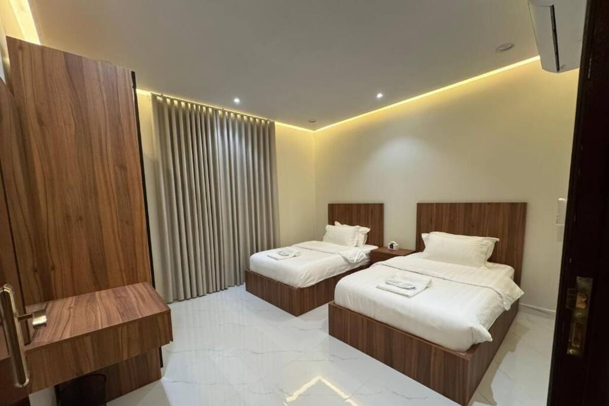 A hotel room with two beds, a wooden vanity, and a modern design.