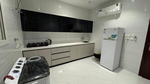 A modern kitchen with white tiles, a black countertop, a built-in stove, a refrigerator, and a black backsplash. - الشقق الفاخره Luxury Apartments (AL Madinah AL Munawwarah)