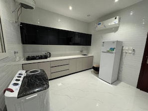 A modern kitchen with white tiles, a black countertop, a built-in stove, a refrigerator, and a black backsplash. - الشقق الفاخره Luxury Apartments (AL Madinah AL Munawwarah)