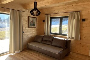 A wooden cabin interior with a sofa, large windows, and a hanging light fixture.