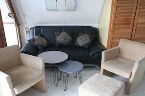 A living area with a dark sofa, two round tables, and two beige armchairs. - Finnish hut Elisabeth (Gager)