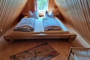 A room with a wooden sloped ceiling, two beds with striped bedding, a window with curtains, and a wooden floor. - Finnish hut Elisabeth (Gager)