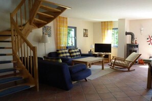 A living room with a sofa, a television, a wooden rocking chair, a fireplace, and a staircase. - Holiday home in Rügen with 2 bedrooms (putgarten)
