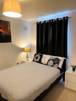 Ein ordentlich gemachtes Bett mit einem gemusterten Überwurf, einer Nachttischlampe, einem schwarzen Kopfteil und einem schwarzen Vorhang.