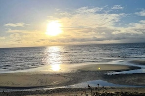 A beach with the sun reflecting on the water, a sandy shore, and some vegetation. - Ostseekieker-Kellenhusen (Kellenhusen)