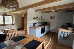 Eine kompakte Küche mit einer zentralen Kochinsel, Holzbalken und einem Essbereich mit Tisch und Stühlen.