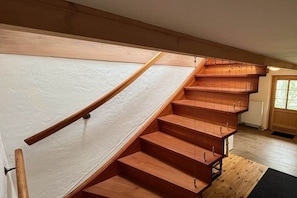 Eine Holztreppe mit Geländer und Metallgriffen, die zu einer Zwischenebene führt.