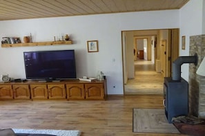 Ein Wohnzimmer mit Fernseher, Holzsäulen, Kamin und einem zur anderen Räumlichkeit führenden Flur.
