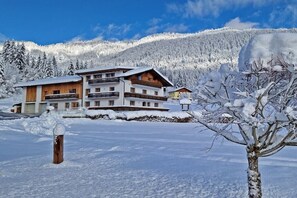 Ein mehrstöckiges Gebäude mit Balkonen, umgeben von schneebedeckten Bäumen und einem Berg im Hintergrund.