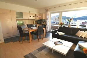 A modern living room with a dining area, a black sofa, and a view of mountains through large windows.