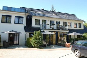 Ein zweistöckiges Gebäude mit Balkon, Außenbereich zum Sitzen und einem geparkten Auto davor.