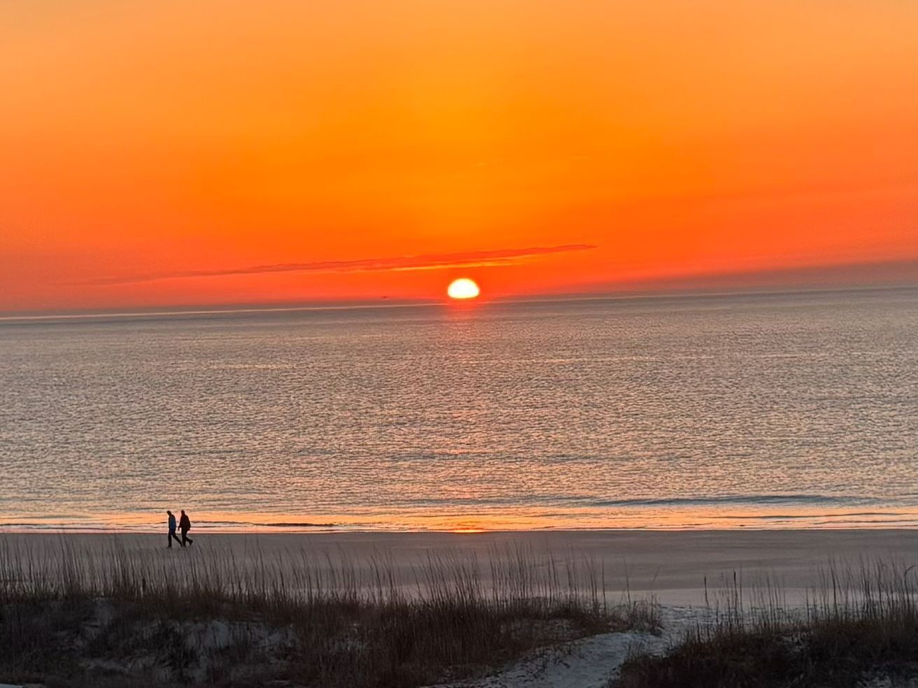 Ein Sonnenuntergang über einem Strand, zwei Personen laufen am Ufer entlang.