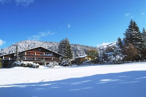 Un refugi amb un edifici gran, arbres coberts de neu i una muntanya al fons.