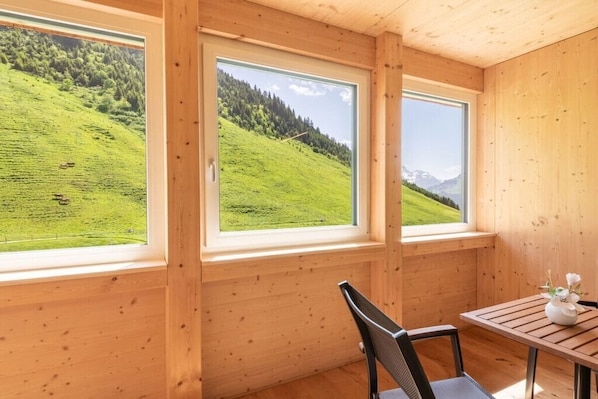 Ein Zimmer mit Holzwänden und großen Fenstern mit Blick auf einen grünen Hügel.