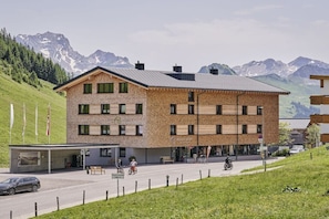 Ein mehrgeschossiges Gebäude mit Backsteinfassade, einem überdachten Eingang und Blick auf Berge im Hintergrund.