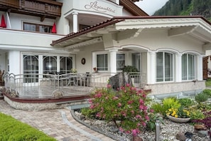 Ein Hotel mit weißer Fassade, einem Balkon mit Metallgeländern und einem Garten mit verschiedenen Pflanzen.