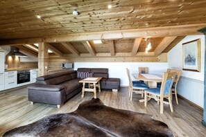 A rustic interior with a wooden ceiling, a sofa, a dining table with chairs, and a kitchen area.
