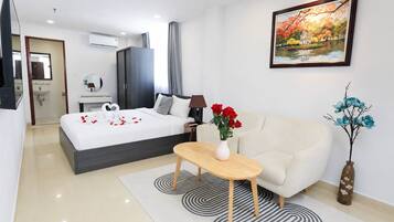 A modern hotel room with a bed, a sofa, a small table, and a painting on the wall.
