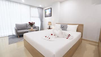 A hotel room with a large bed, a grey sofa, a small table with a vase of red roses, and a painting on the wall.