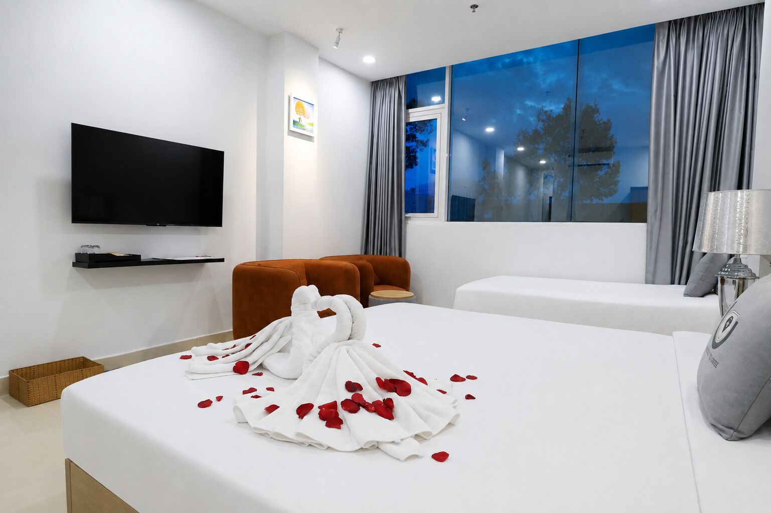 A hotel room with a bed, a TV, a sofa, and a window with curtains.