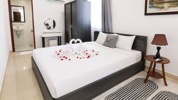 A hotel room with a large bed, a bedside table with a lamp, a wardrobe, a bathroom, and a painting on the wall.