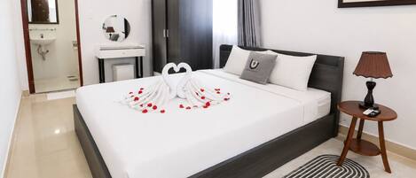 A hotel room with a large bed, a bedside table with a lamp, a wardrobe, a bathroom, and a painting on the wall.