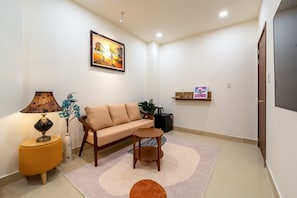 A living room with a sofa, a small round table, a lamp, a vase with flowers, and a painting on the wall.