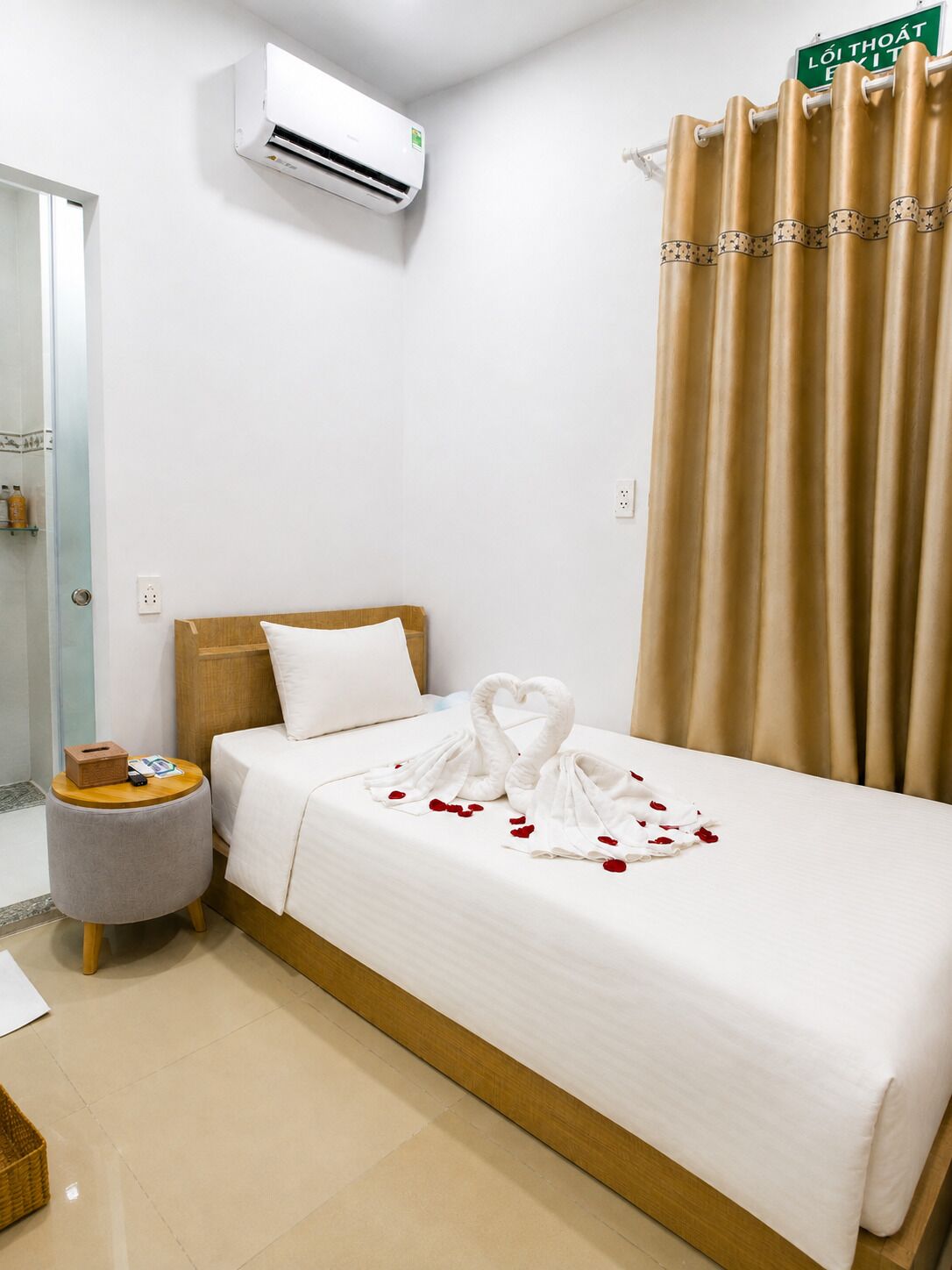 A hotel room with a bed, an air conditioning unit, a curtain, and a sign indicating the exit.