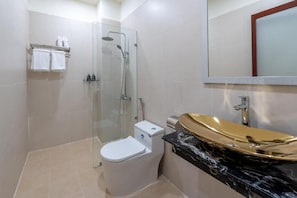 A bathroom with a glass-enclosed shower, a white toilet, a gold vanity, and a mirror above the sink.