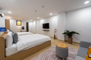 A modern hotel room with a bed, a TV, a small table, and a plant.
