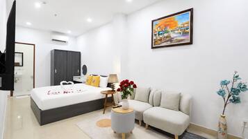 A modern hotel room with a large bed, a sofa, a small round table, and a painting on the wall.