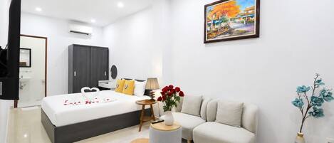 A modern hotel room with a large bed, a sofa, a small round table, and a painting on the wall.