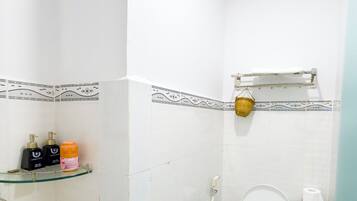 A small, clean bathroom with a toilet, a glass shelf with toiletries, and a shower area.