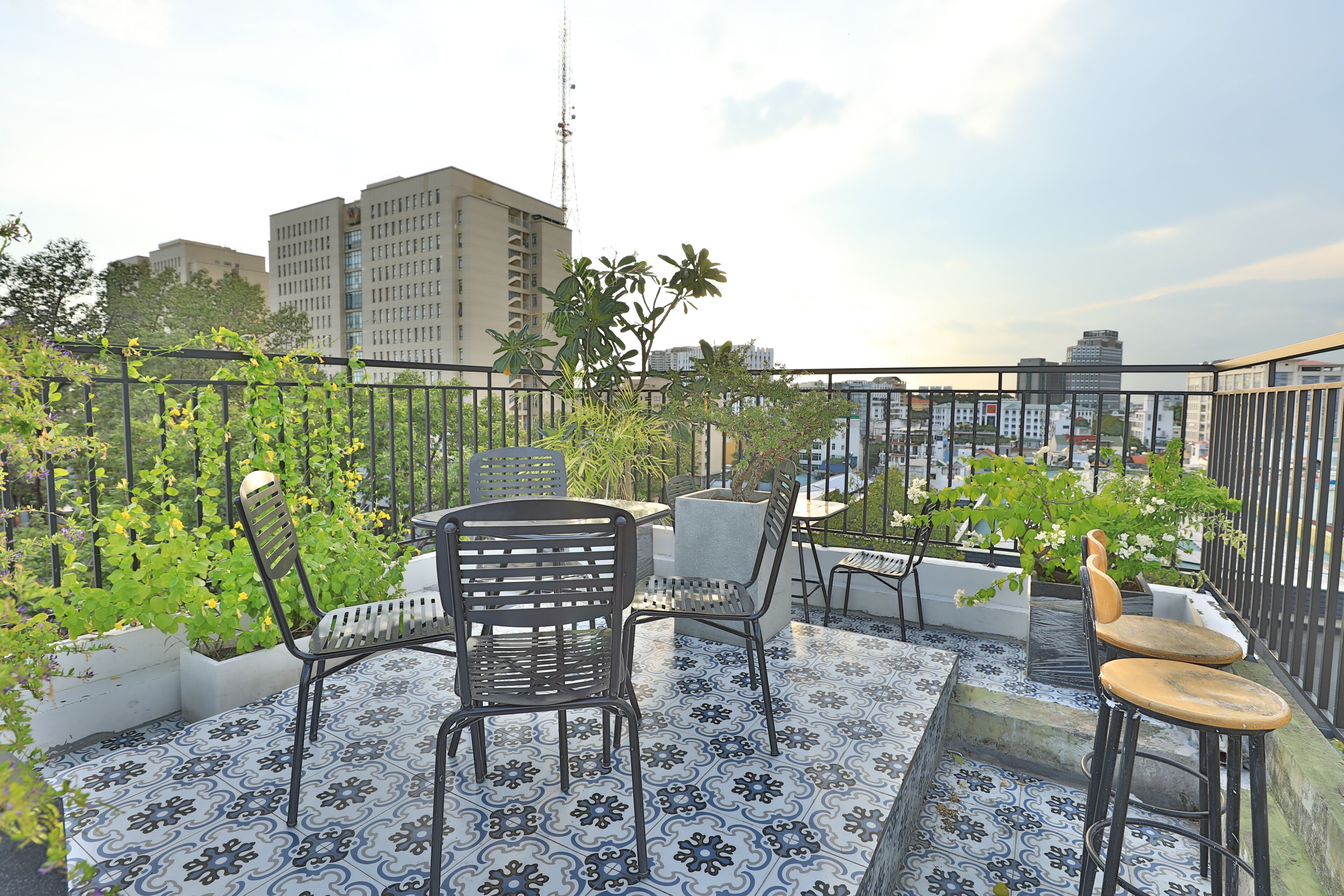 A rooftop terrace with outdoor seating, a patterned floor, and a view of the cityscape.