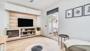 A modern living room with a flat-screen TV, wooden flooring, a round rug, a sofa, and a dining area visible through a glass door. - Bakea Home Gran Canaria. 10mins from the beach and the airport. (Ingenio)