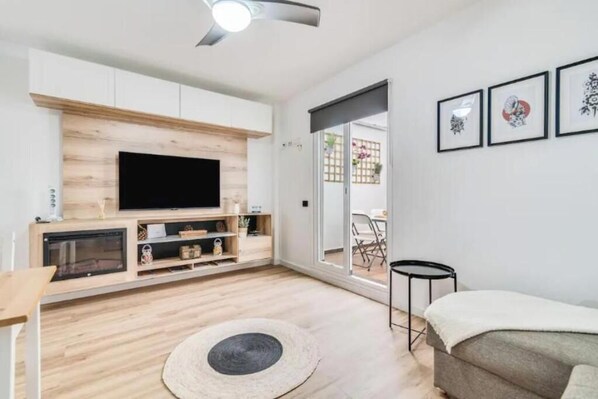 A modern living room with a flat-screen TV, wooden flooring, a round rug, a sofa, and a dining area visible through a glass door. - Bakea Home Gran Canaria. 10mins from the beach and the airport. (Ingenio)