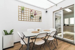 A conference room with a white table, four chairs, a grid wall with potted plants, and a sliding glass door to a kitchen area. - Bakea Home Gran Canaria. 10mins from the beach and the airport. (Ingenio)