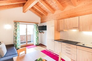 A compact kitchen with wooden cabinets, a dining table with chairs, and a sliding glass door leading to an outdoor area. - Rothorn - App. Braunarl (Schröcken)