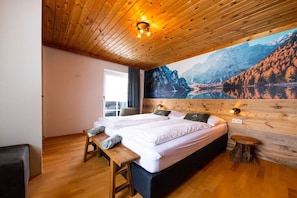 Ein Schlafzimmer mit zwei Betten, Holzboden, einem großen Bergbild und einem kleinen hölzernen Hocker.
