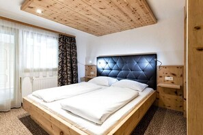 Ein Doppelbett mit einem gepolsterten Kopfteil, Holzpaneelen am Kopfteil, einem Heizkörper und einem Fenster mit durchscheinenden Vorhängen.