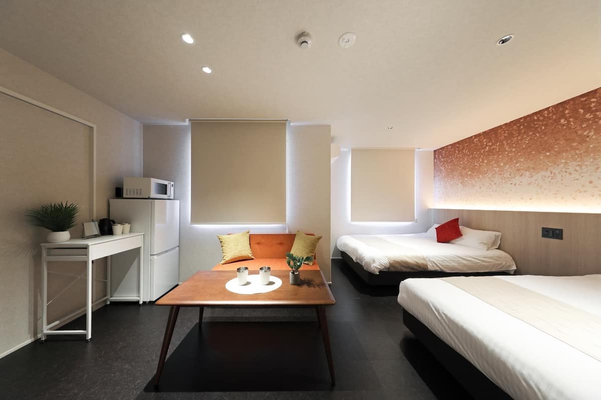 Habitación de hotel compacta con kitchenette, una pequeña mesa de comedor, dos camas y un ventanal grande.