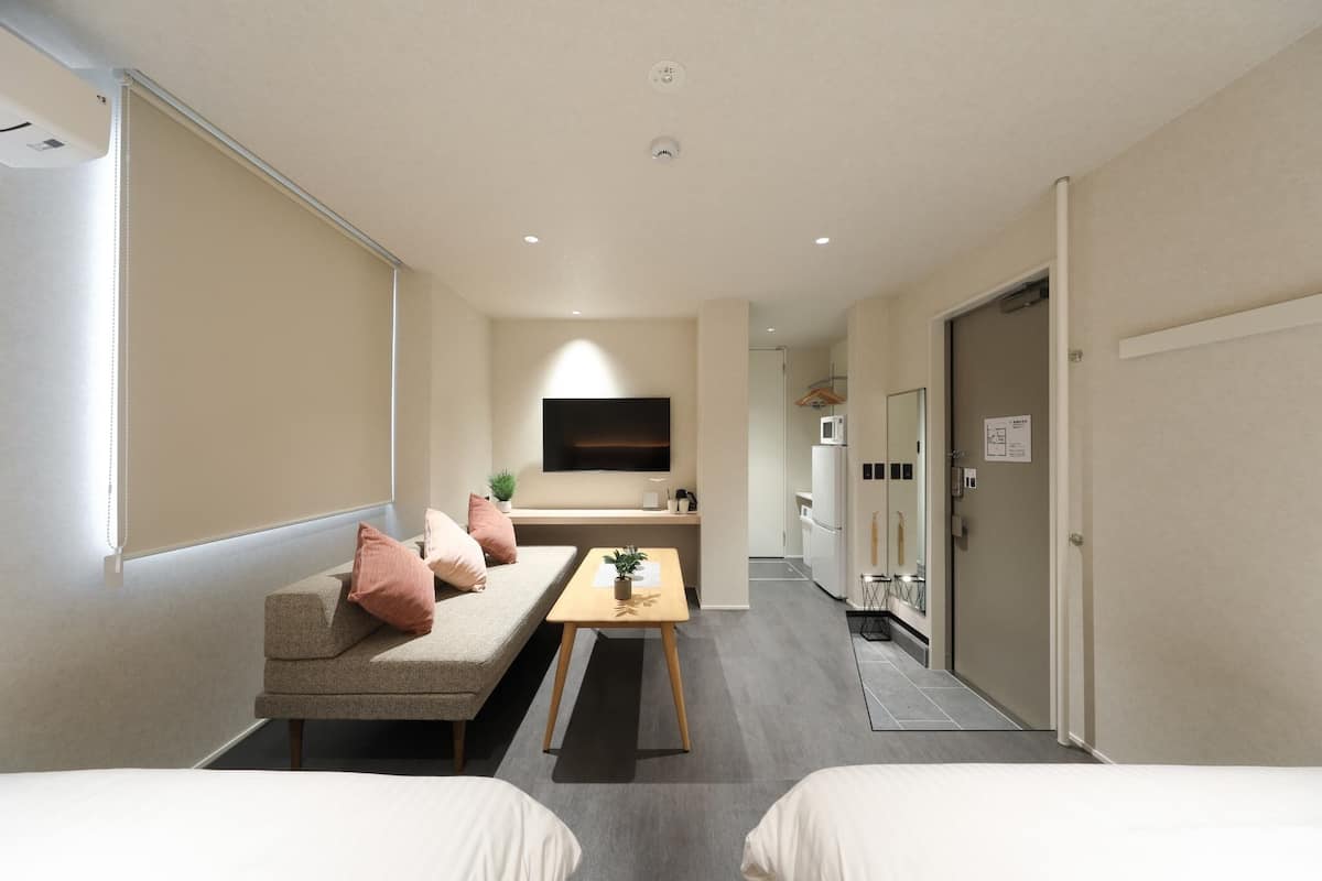 Una habitación de hotel moderna con sofá, una mesita, televisión, kitchenette y puerta.