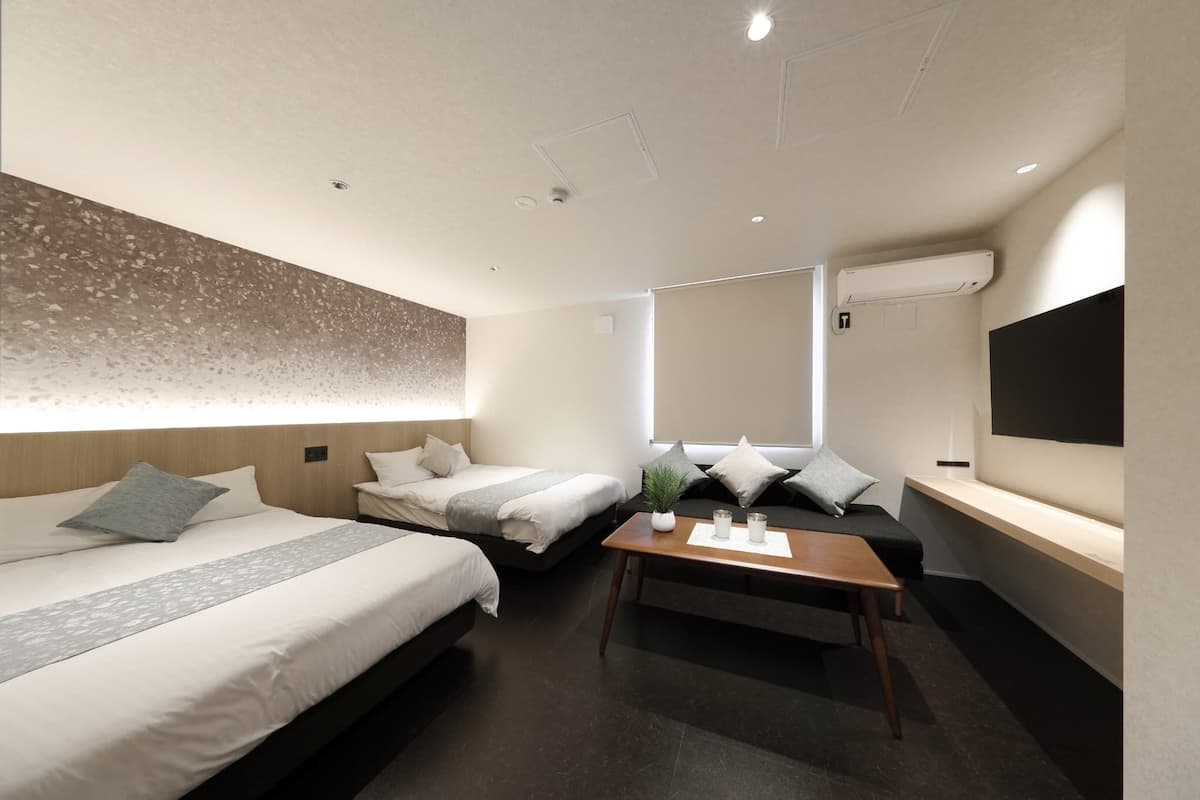 Una habitación de hotel moderna con dos camas, un sofá, una mesita de café y un televisor montado en la pared.