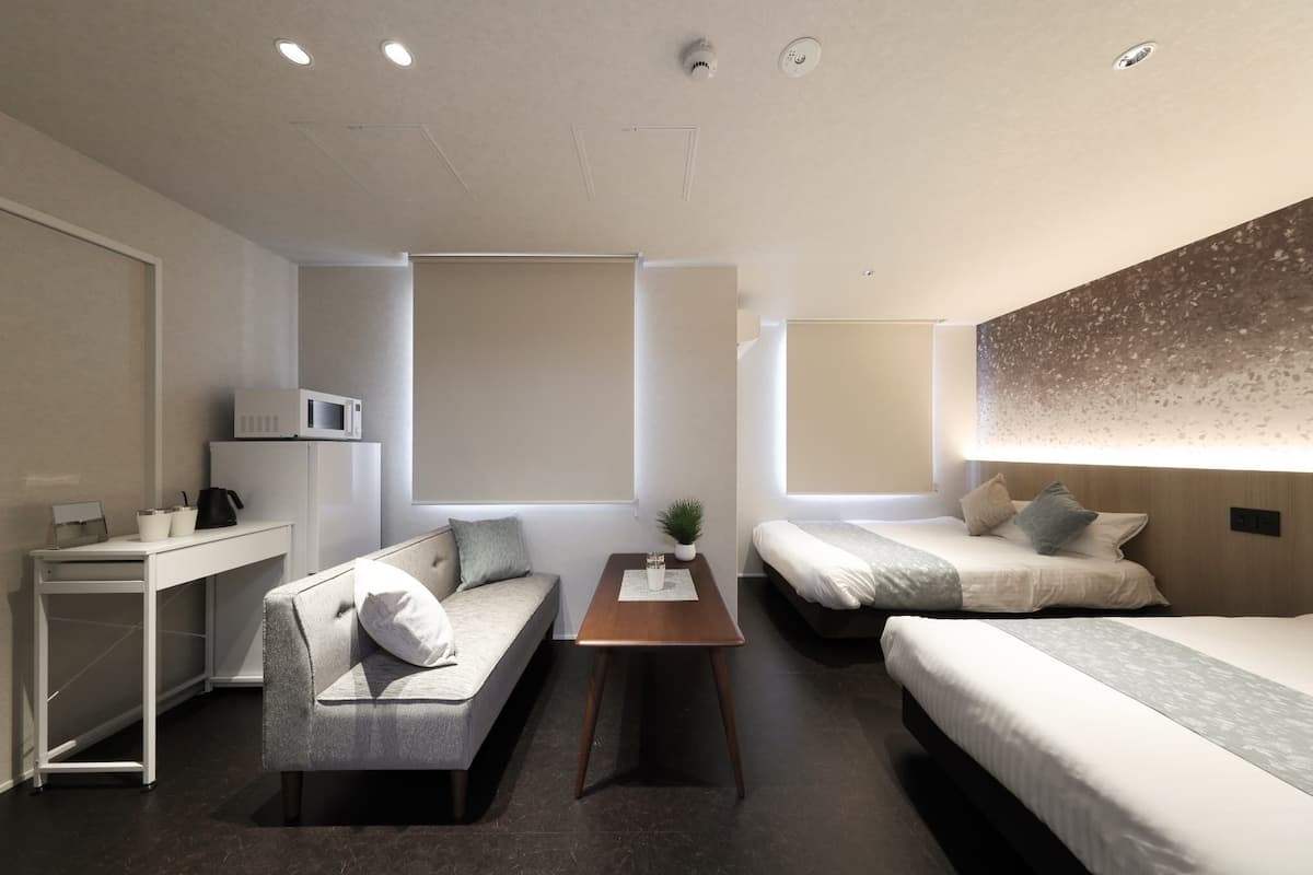 Una habitación de hotel moderna con un sofá, dos camas individuales, una mesita pequeña, un microondas y un escritorio.