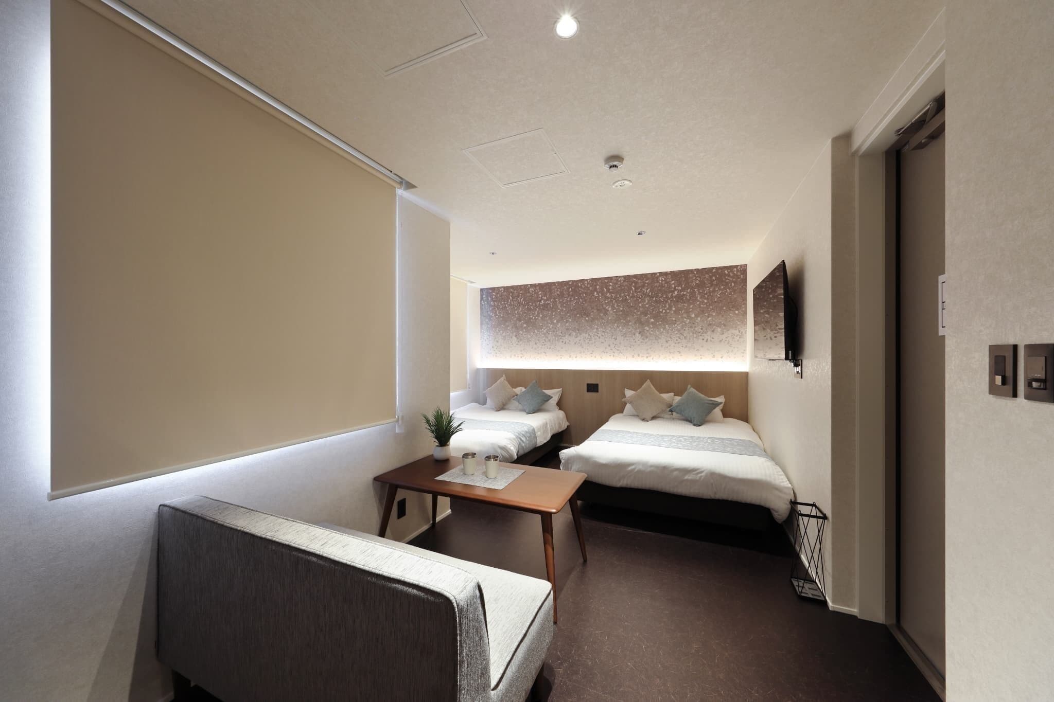 Quarto de hotel pequeno com cama, mesa de cabeceira e um cantinho de estar.