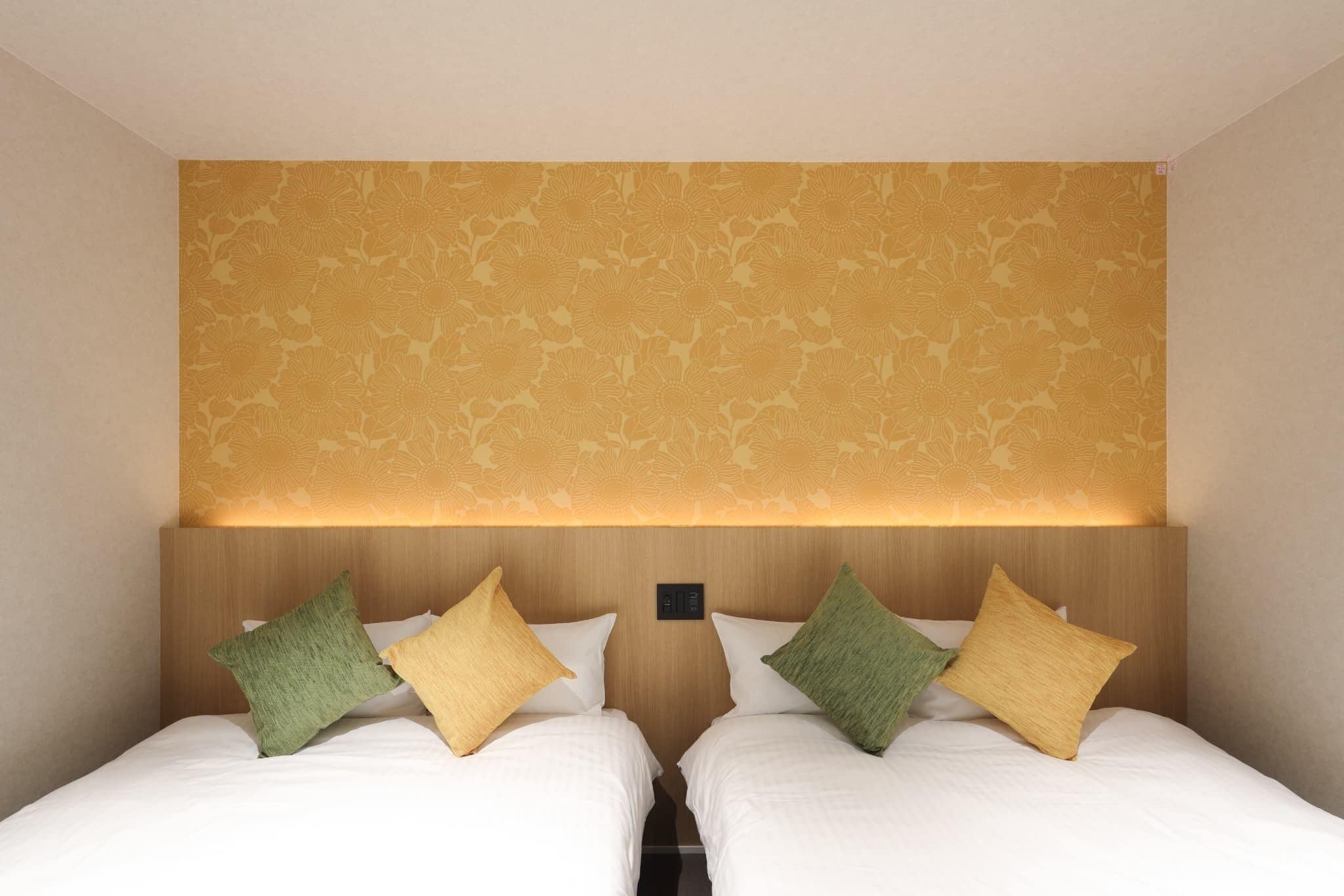 Una camera d'albergo con due letti, una parete decorata e una testiera con una lampada.