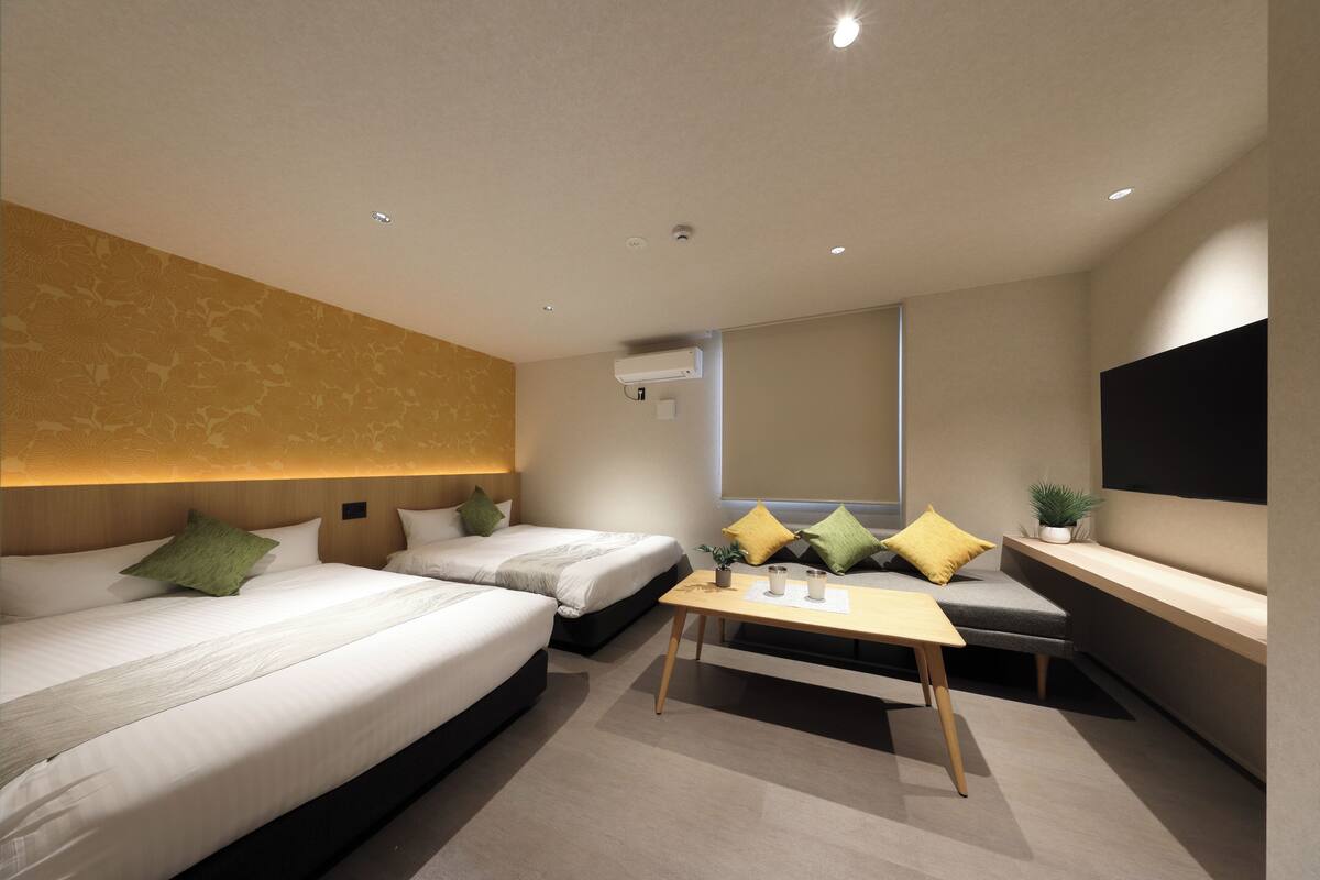 Una habitación de hotel moderna con dos camas, una mesita, un sofá, un televisor y una ventana.